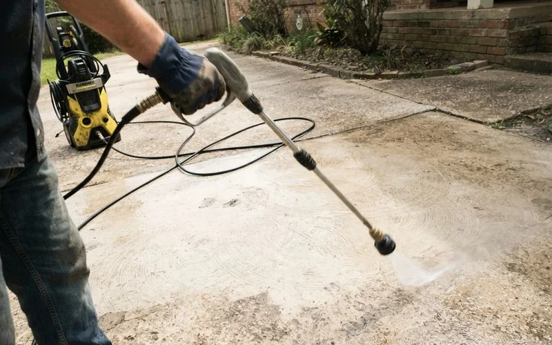 A pressure washer nozzle held too close to concrete, showing the early stage of an etched or striped surface